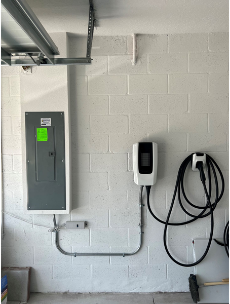 Electrical panel and EV charger installed on a white cinder block garage wall.