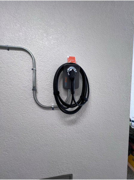 Electric vehicle charger mounted on a textured wall, with black charging cable and conduit.