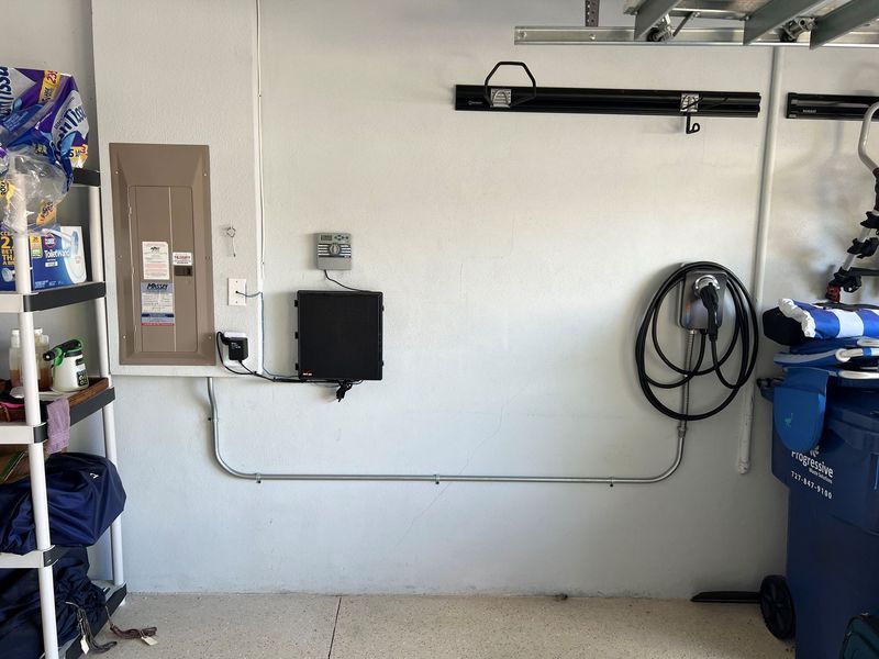 Garage wall with electrical panel, charger box, conduit, and EV charger cable.