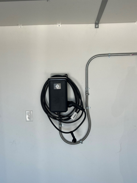 Black electric vehicle charger mounted on a white wall, with a silver conduit.
