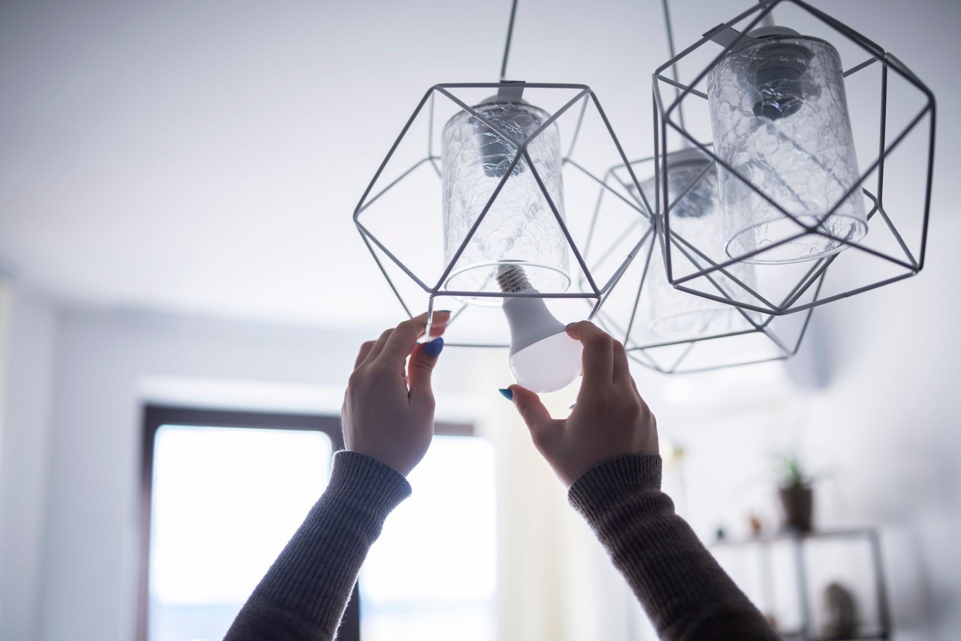 Person replacing a lightbulb in a geometric pendant lamp indoors.