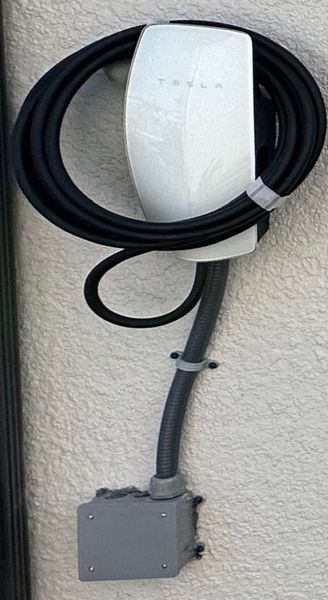 White Tesla wall charger with black cable mounted on a textured wall.