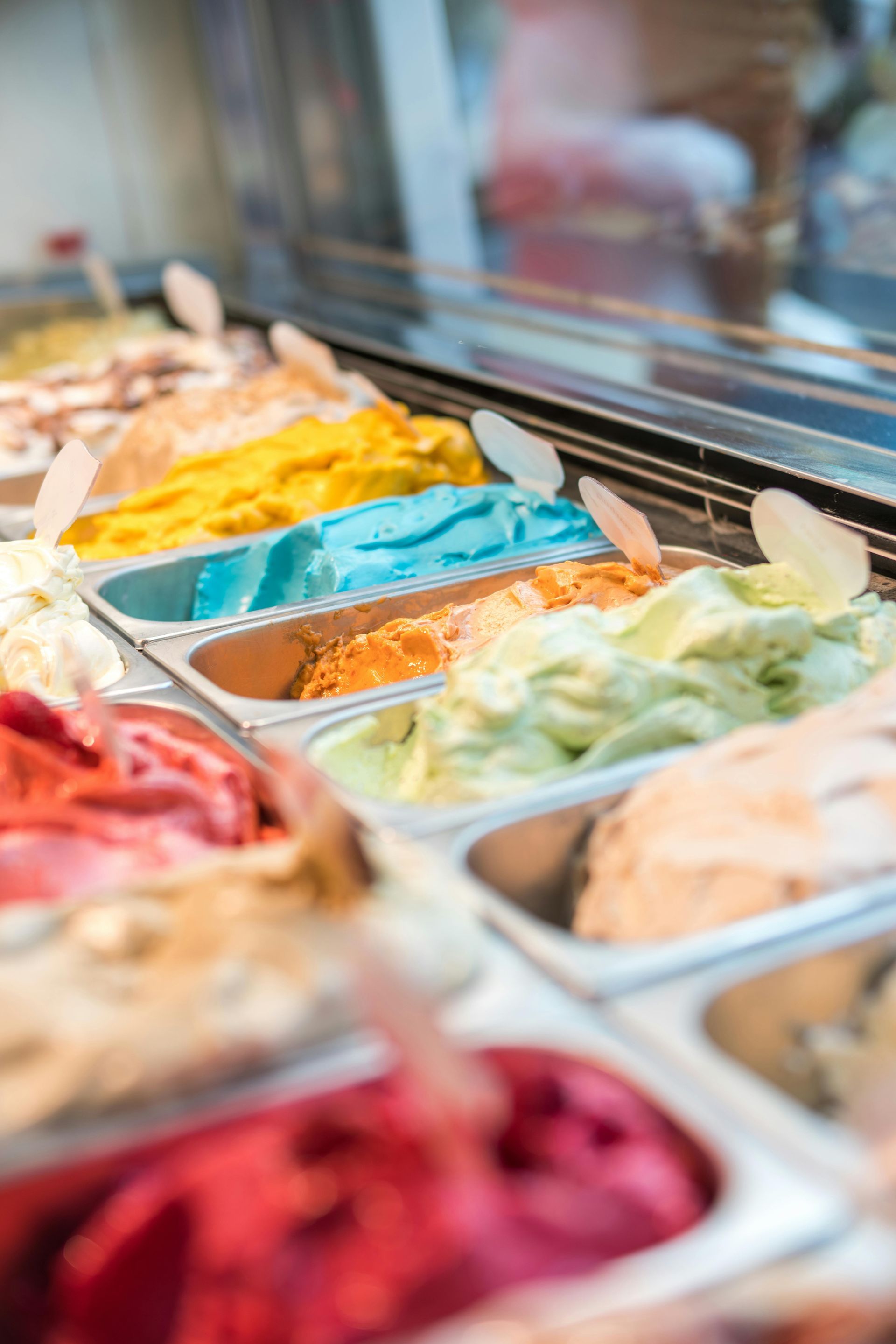 Display case with colorful gelato scoops, including red, yellow, blue, and green, in an ice cream shop.