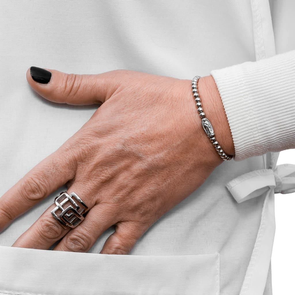 Mano con esmalte de uñas negro, anillo y pulsera en el bolsillo de una bata blanca.