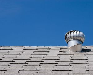 A wind turbine on top of a roof with a blue sky in the background.