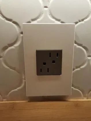 Gray electrical outlet on white plate; mounted on tile wall.