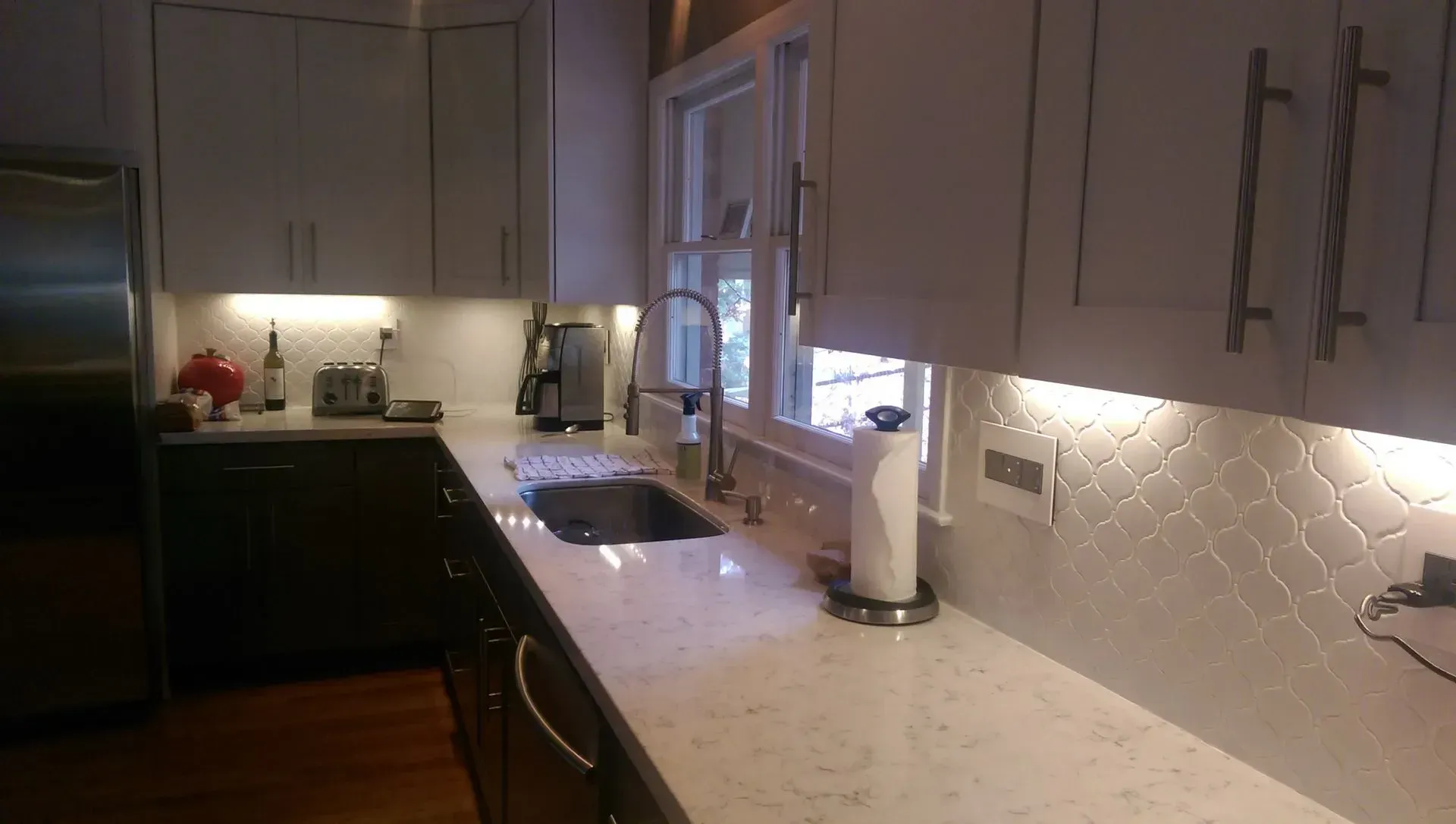 Modern kitchen with white cabinets, light countertops, and patterned backsplash.