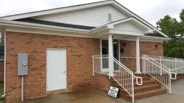 Brick building with white door, porch with stairs, and a metal box on the wall.