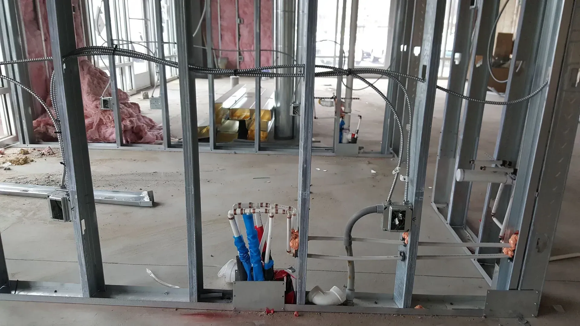 Interior of a building under construction, metal stud framing. Electrical wiring and pink insulation visible.