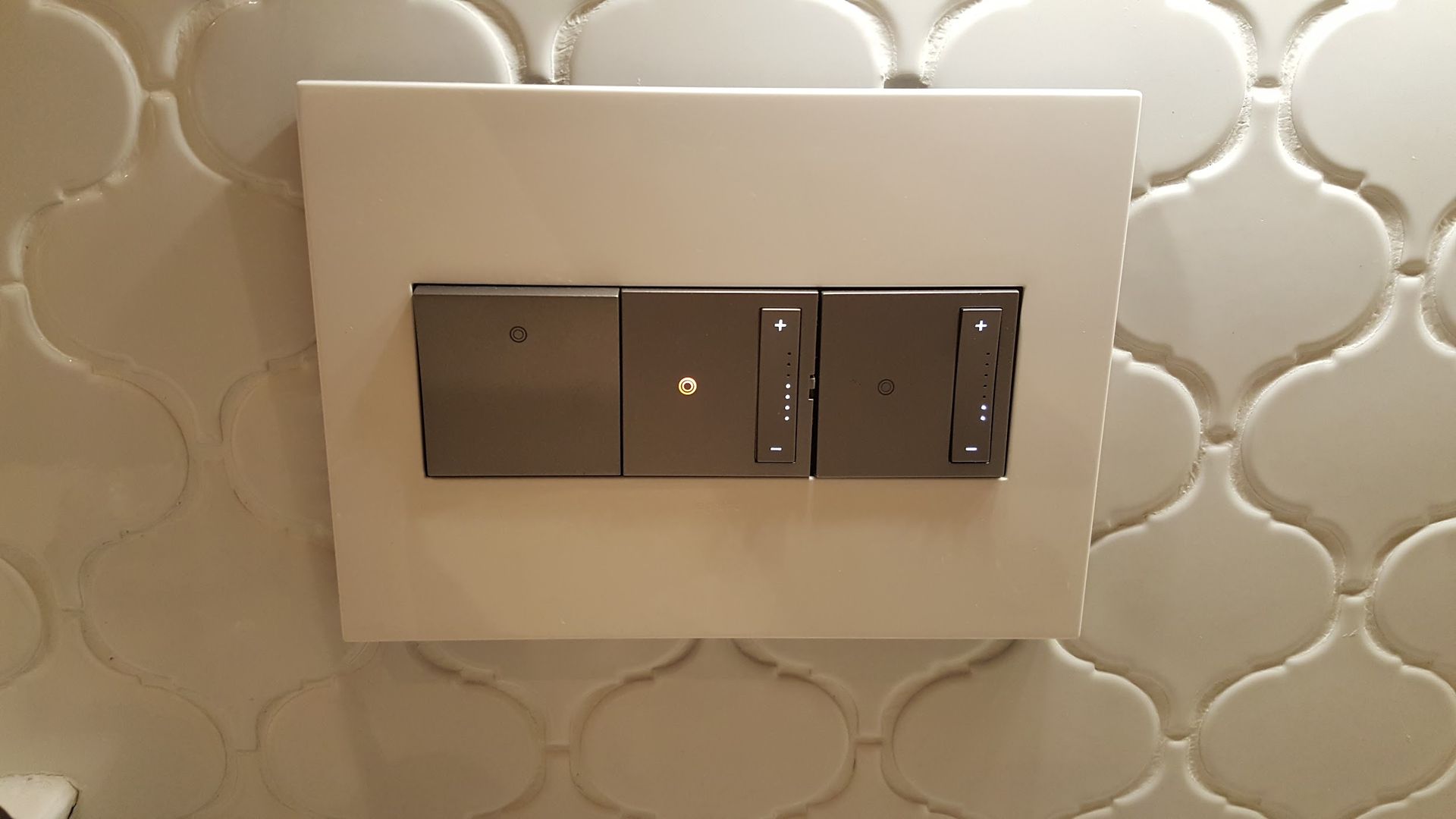 Gray light switch controls on a white tiled wall.