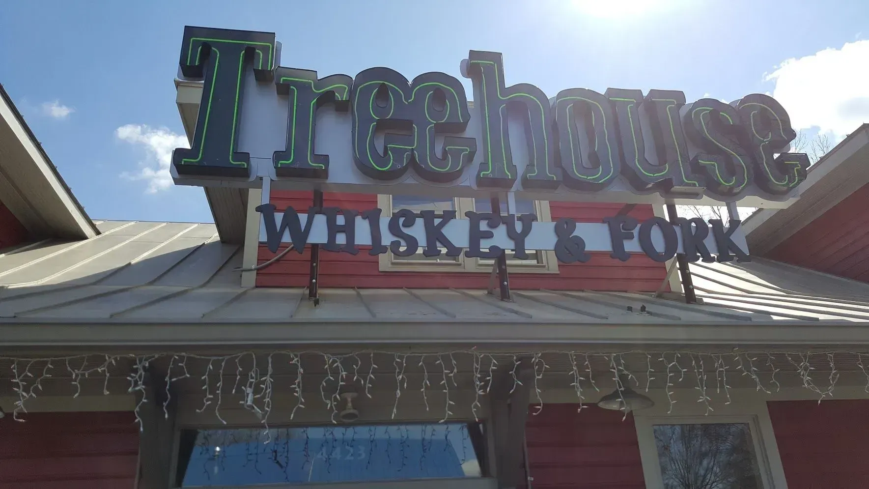 Treehouse Whiskey & Fork restaurant sign. Green neon lettering on red building with blue sky.