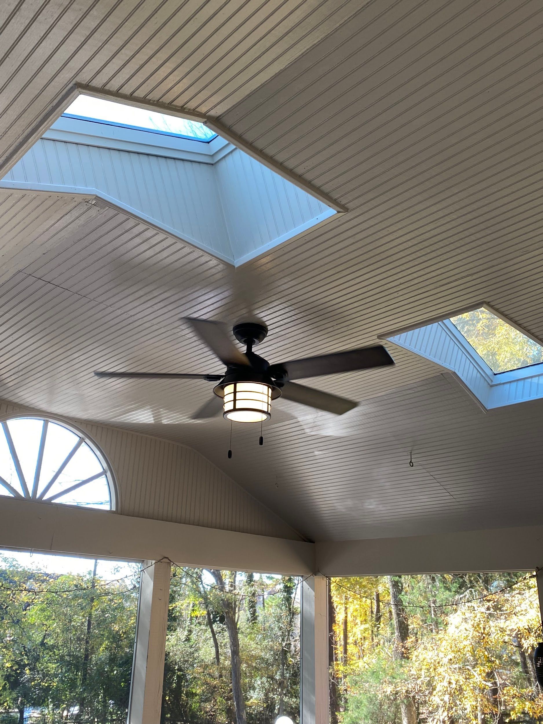 Ceiling with skylights, fan, and outdoor view. Beige ceiling with three skylights, fan with light, and trees visible.