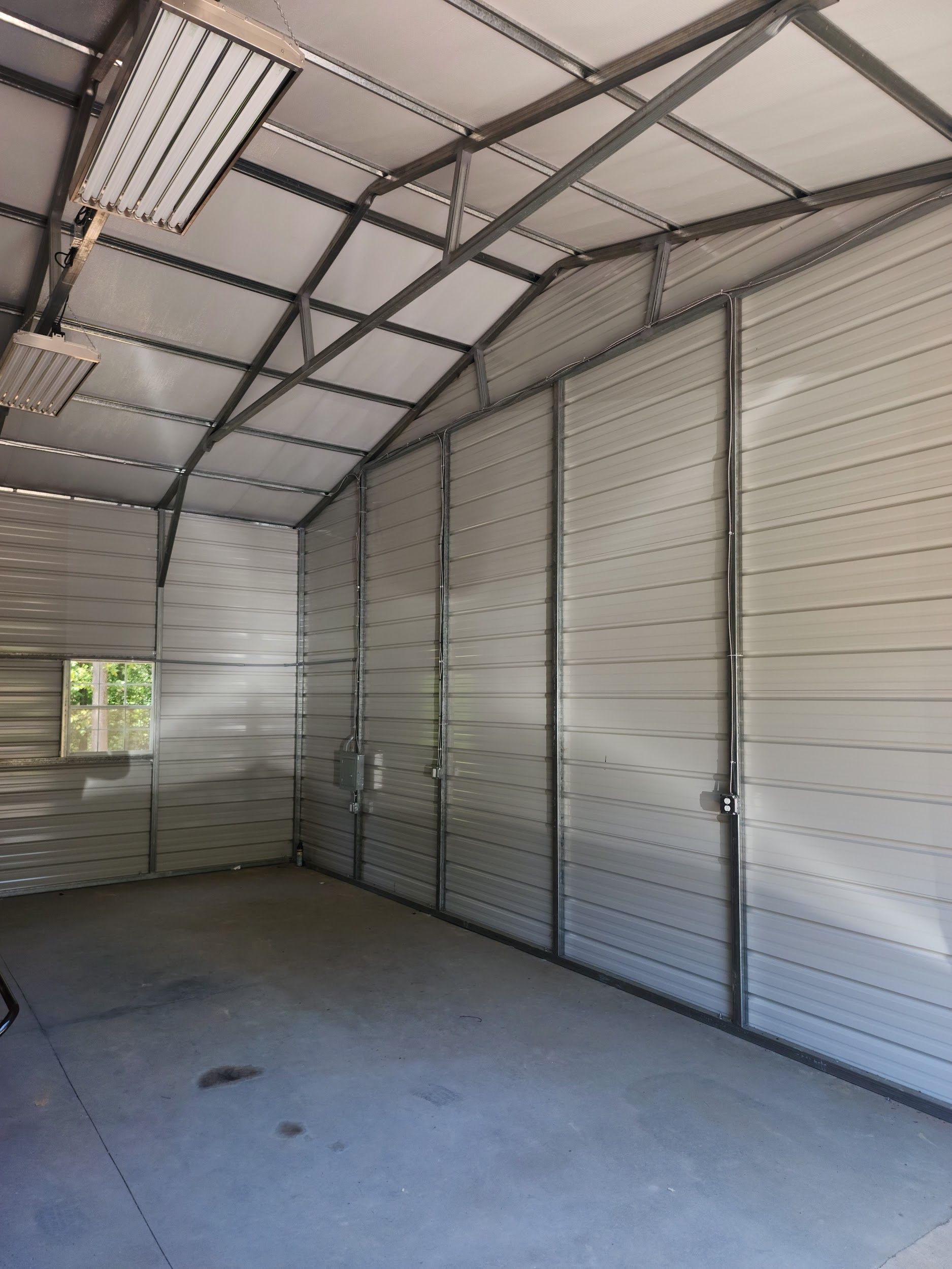 Interior of a metal building with a concrete floor, a window, and closed double doors.
