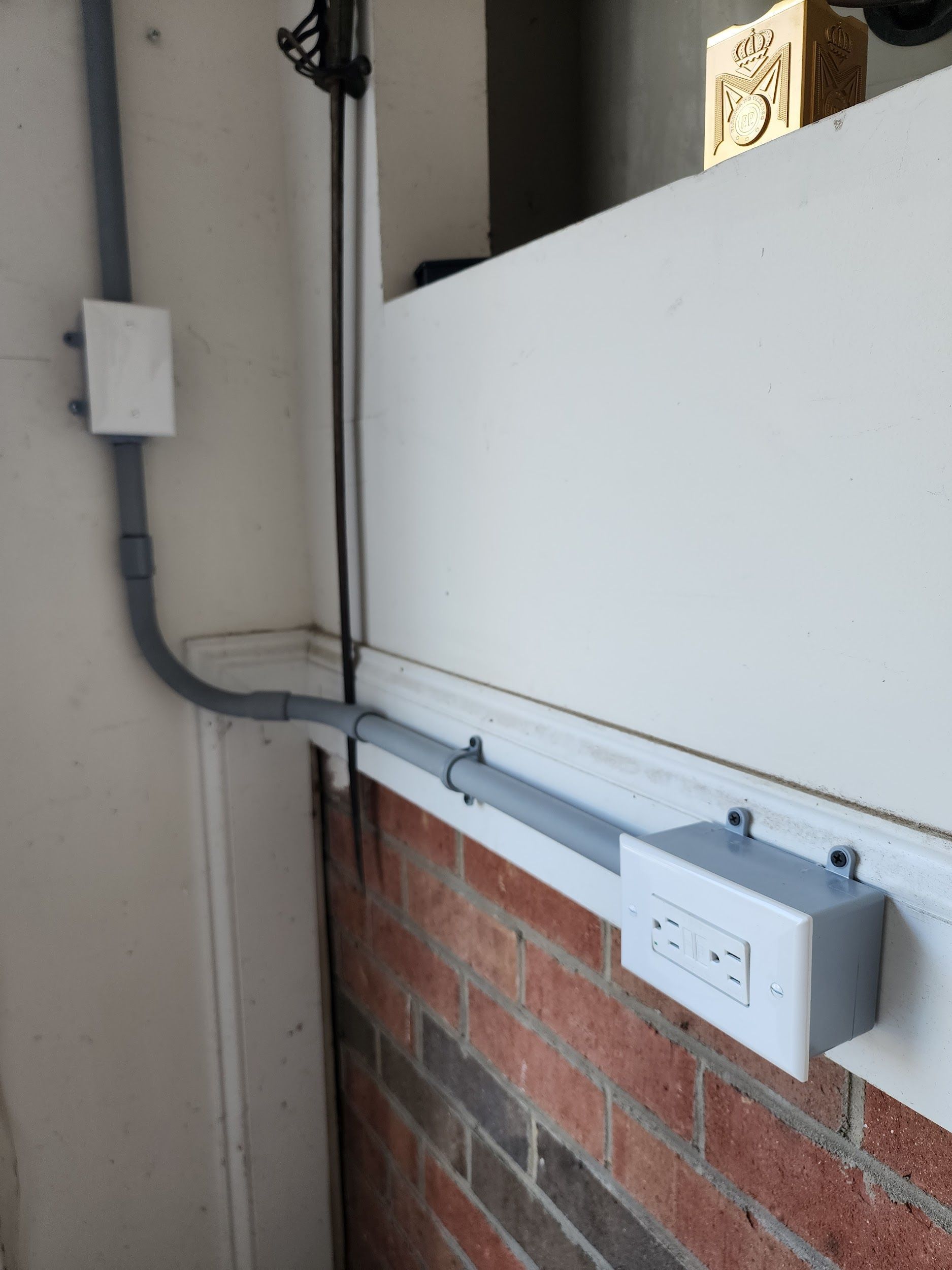 Gray electrical conduit and boxes run along a brick wall and up a white wall.