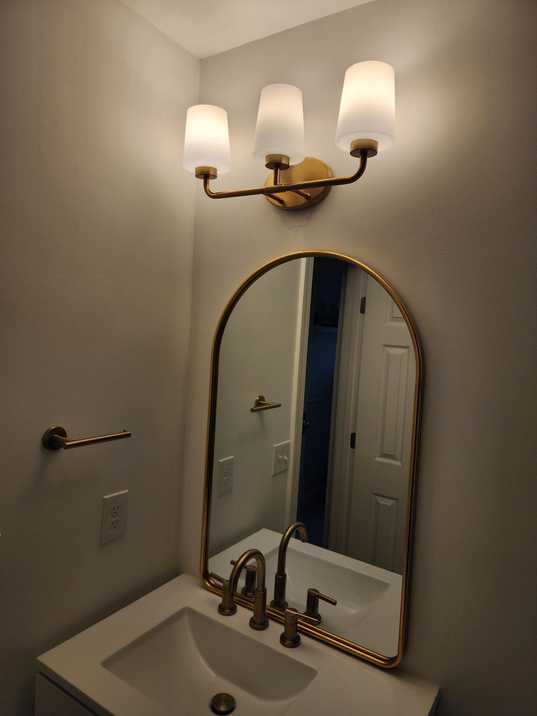 Bathroom with a gold-framed arched mirror, a three-light fixture, and gold fixtures.