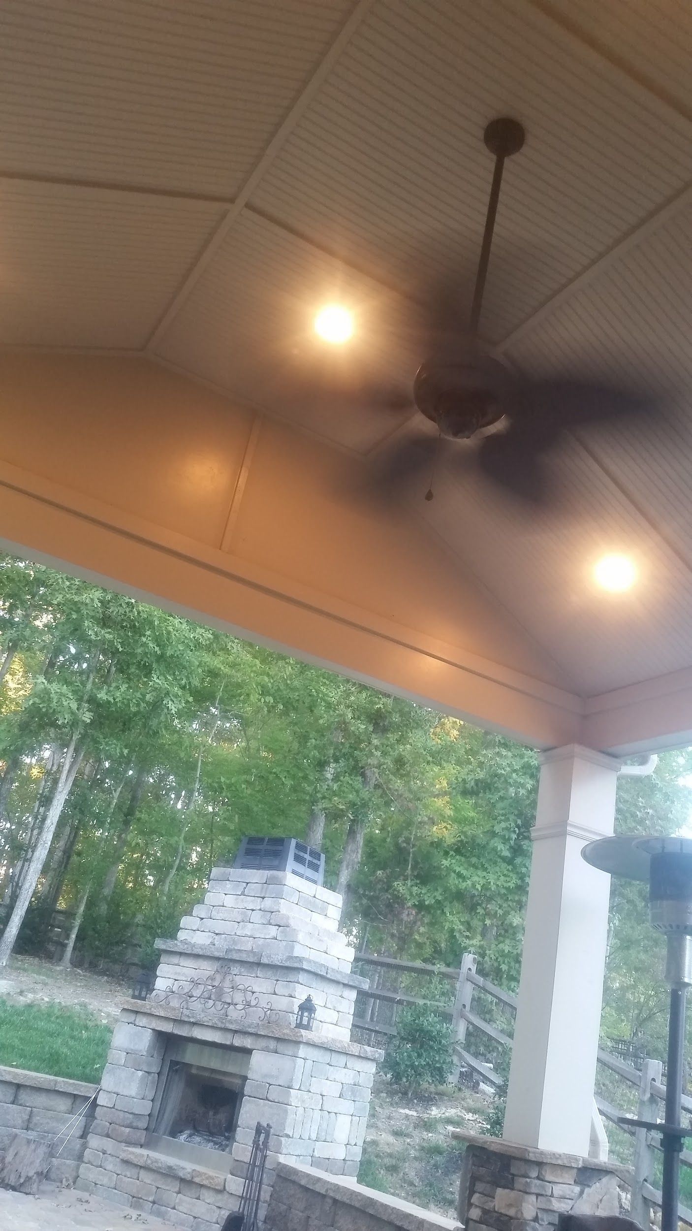 Covered outdoor patio with ceiling fan and fireplace.