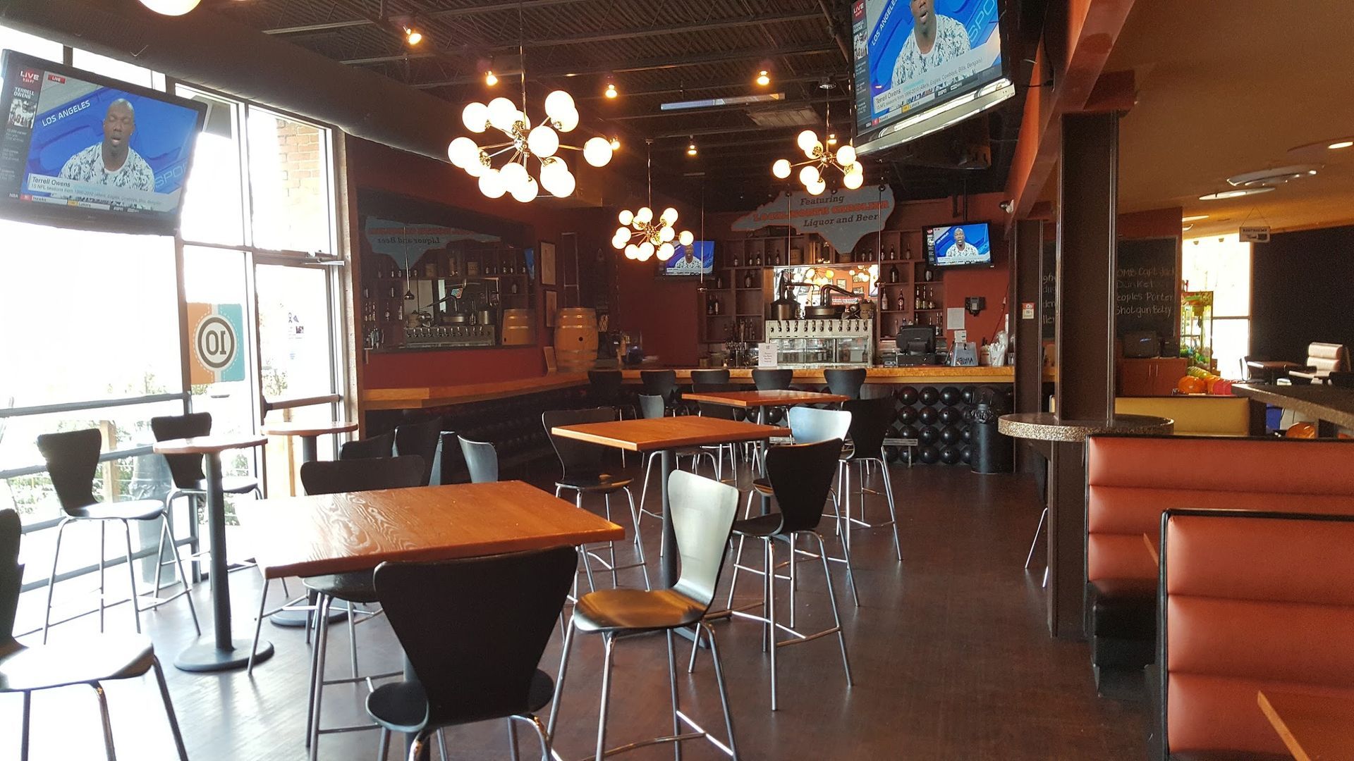Interior of a restaurant with tables, chairs, bar, TVs, and decorative lights.