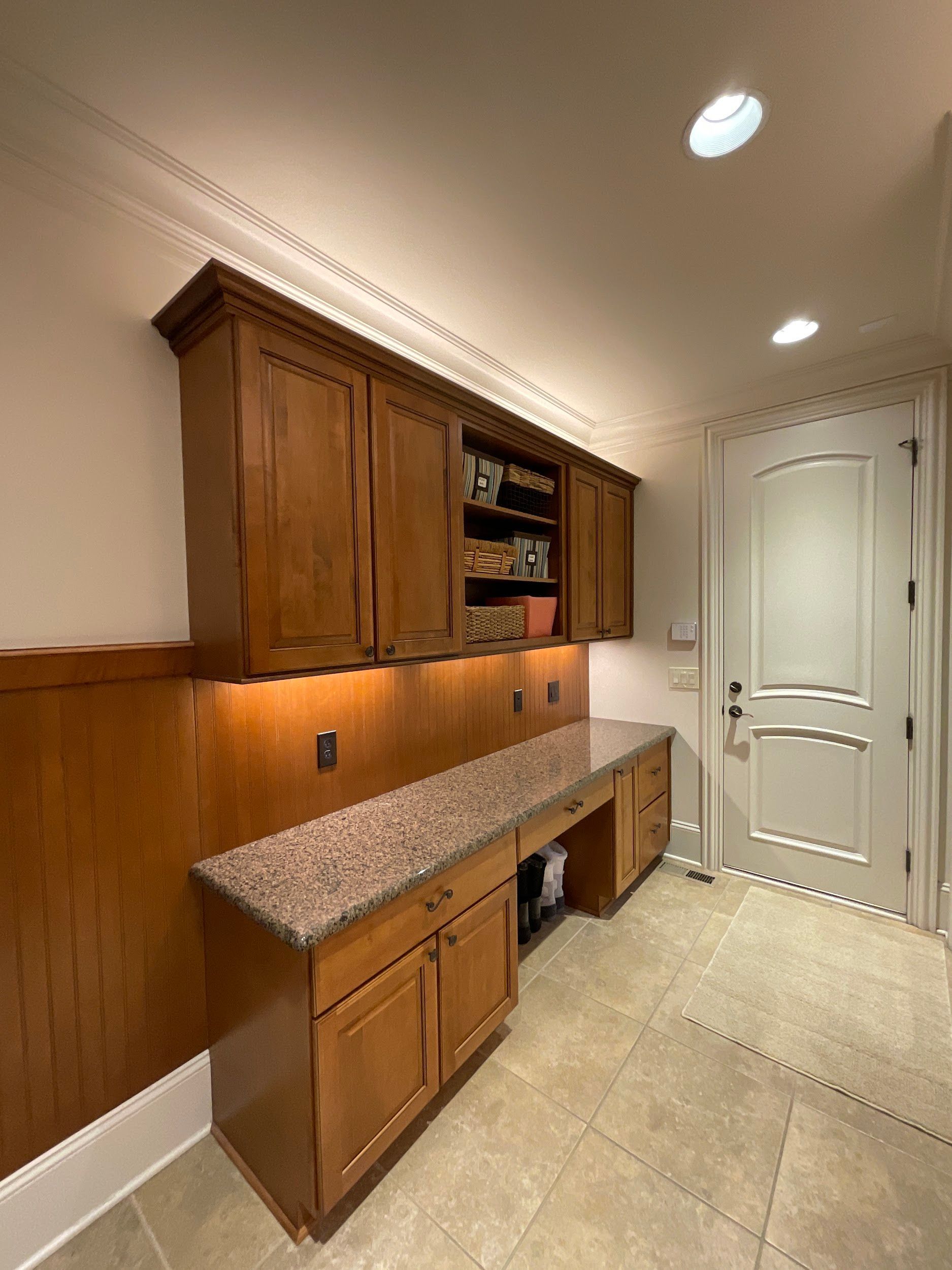 Wooden cabinetry and granite countertop workspace with door in a well-lit room.