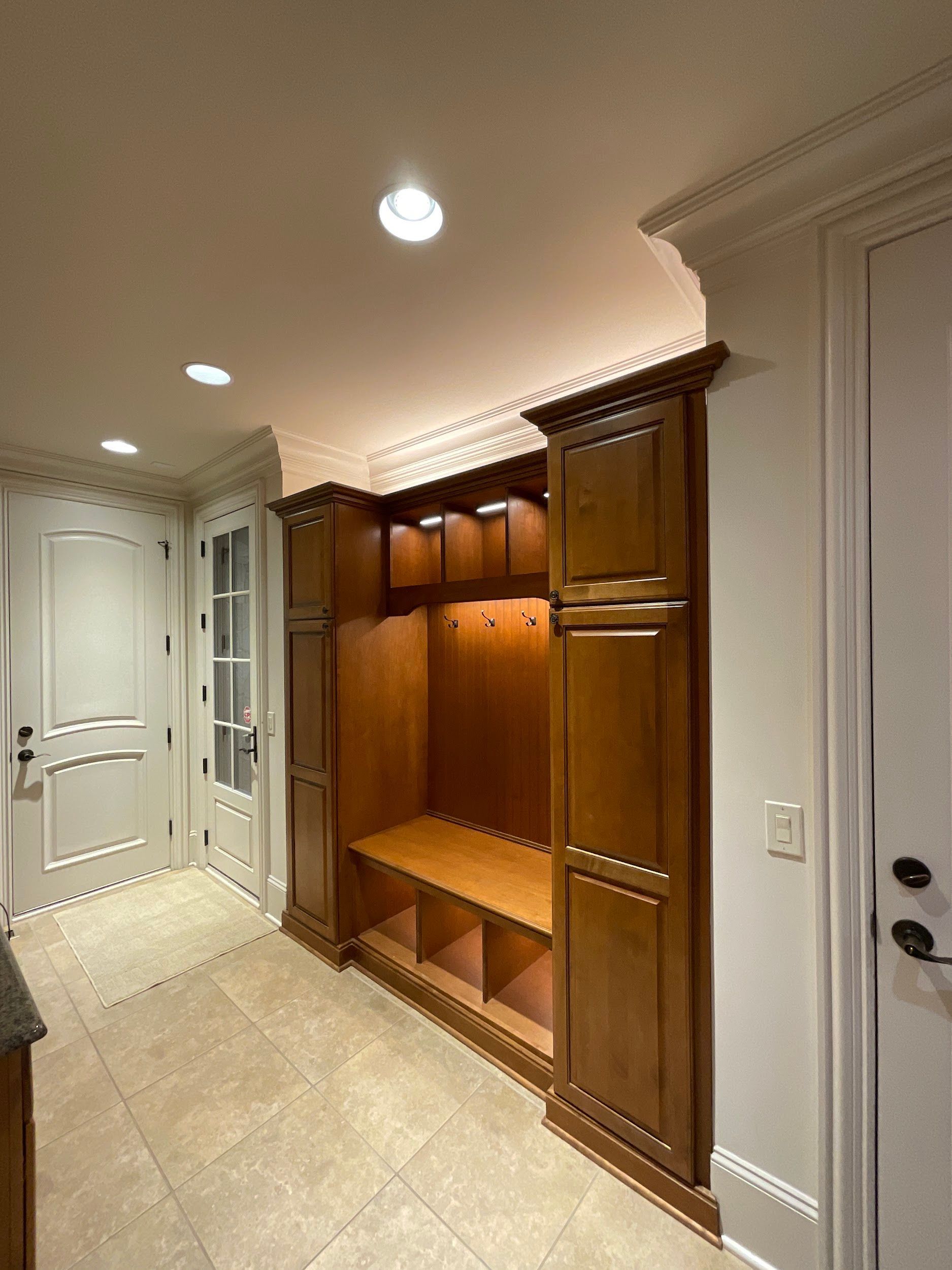 Mudroom with built-in wooden storage, bench, and hooks, near a door.
