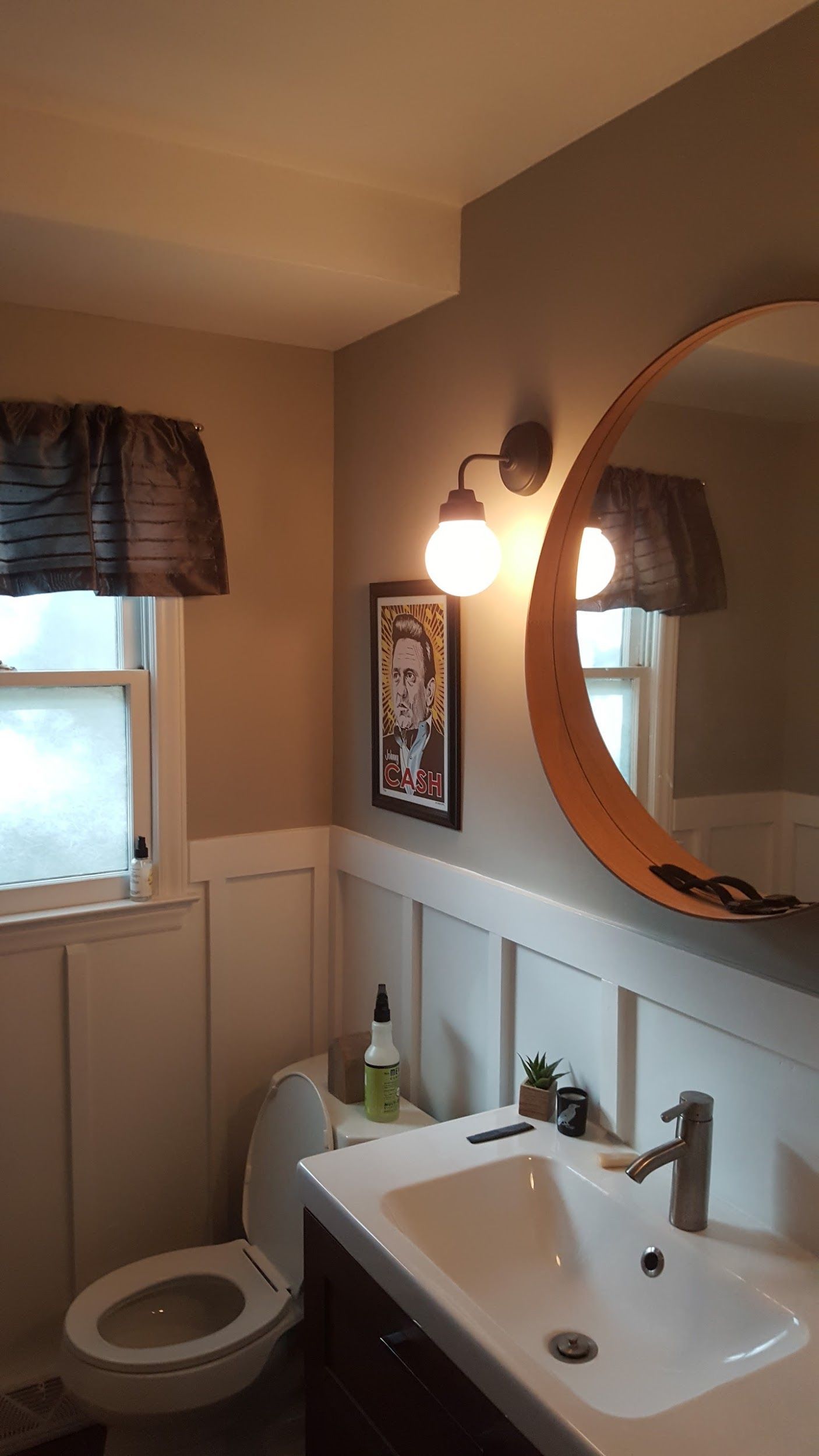 Bathroom with white wainscoting, a round mirror, and a wall-mounted light fixture.
