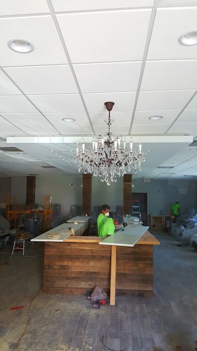 A chandelier hangs in a room under construction, with workers at a bar.