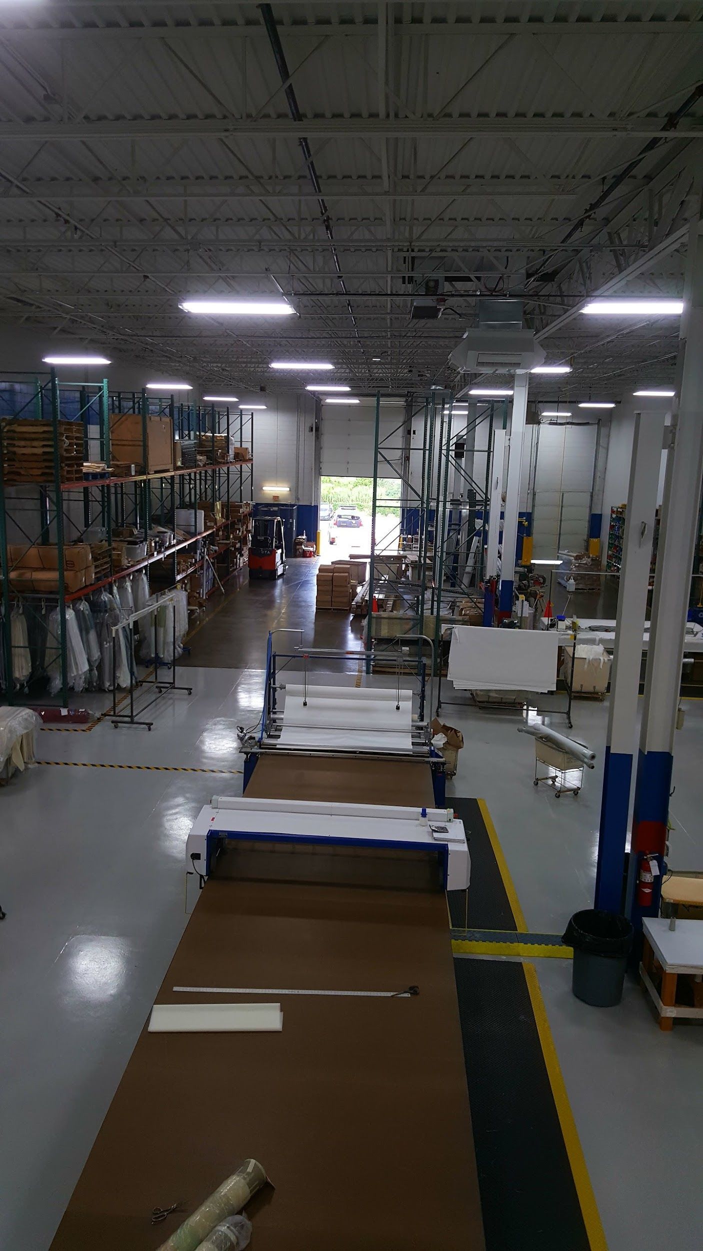 Warehouse interior with shelving, machinery, and open loading door; forklift in the distance.