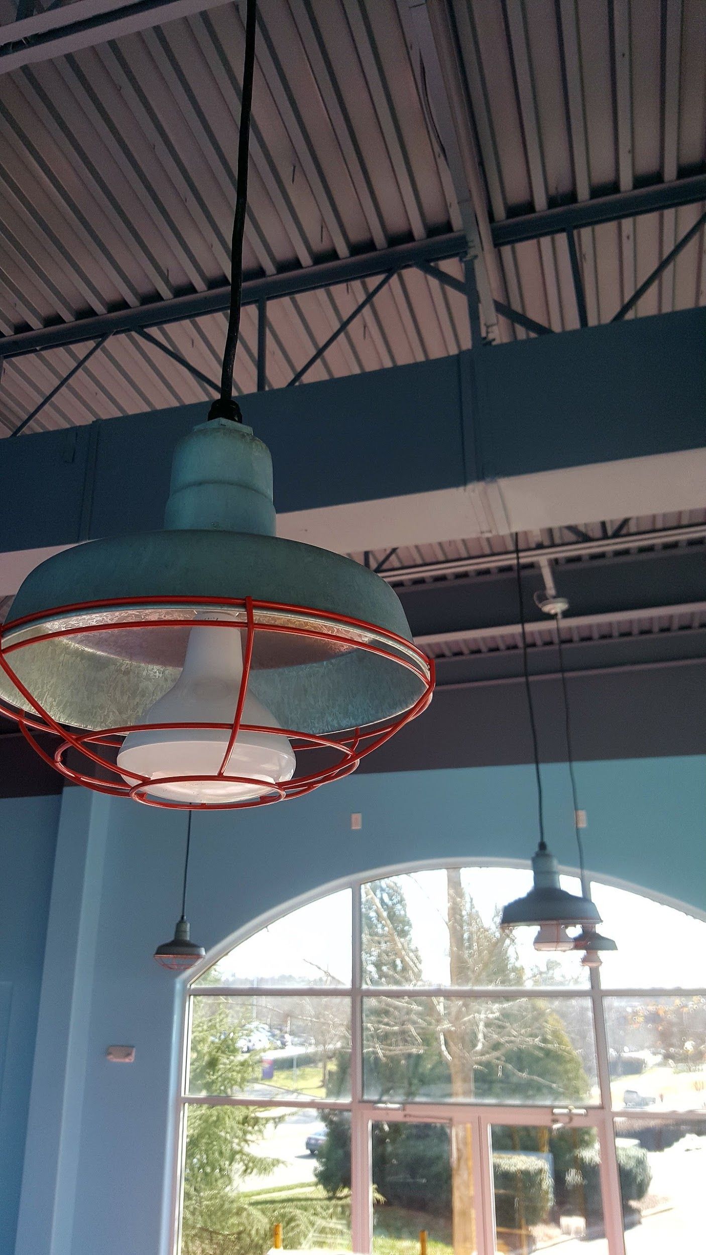 Teal industrial pendant light with red cage over a large window and blue wall.