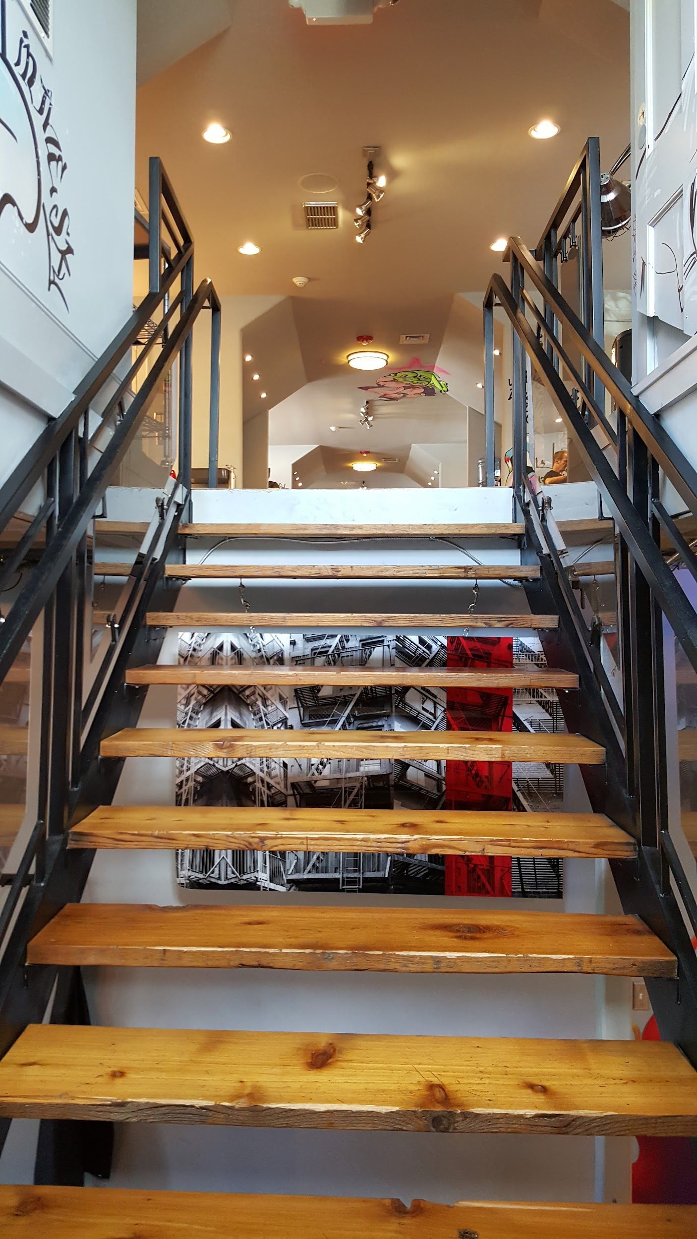 Wooden staircase with black metal railings, leading to a bright hallway with recessed lighting.