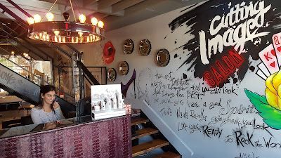 Woman at reception desk in a hair salon. Graffiti art on the wall with stairs and a chandelier.