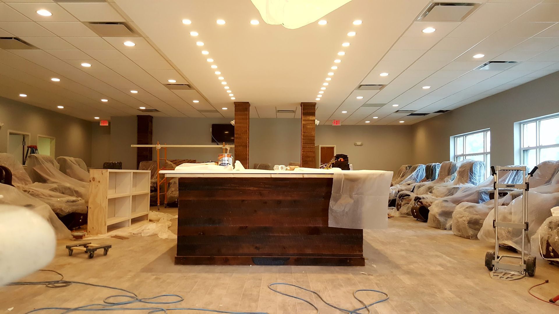 Interior of a commercial space under construction: wooden bar, covered chairs, exposed ceiling lights.