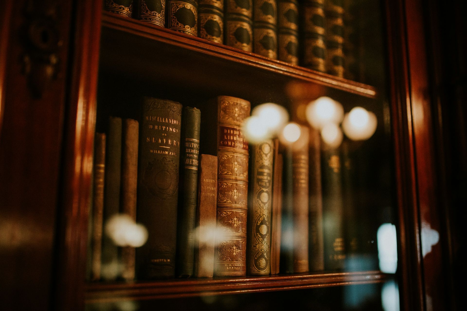 A shelf filled with lots of old books in a glass case.