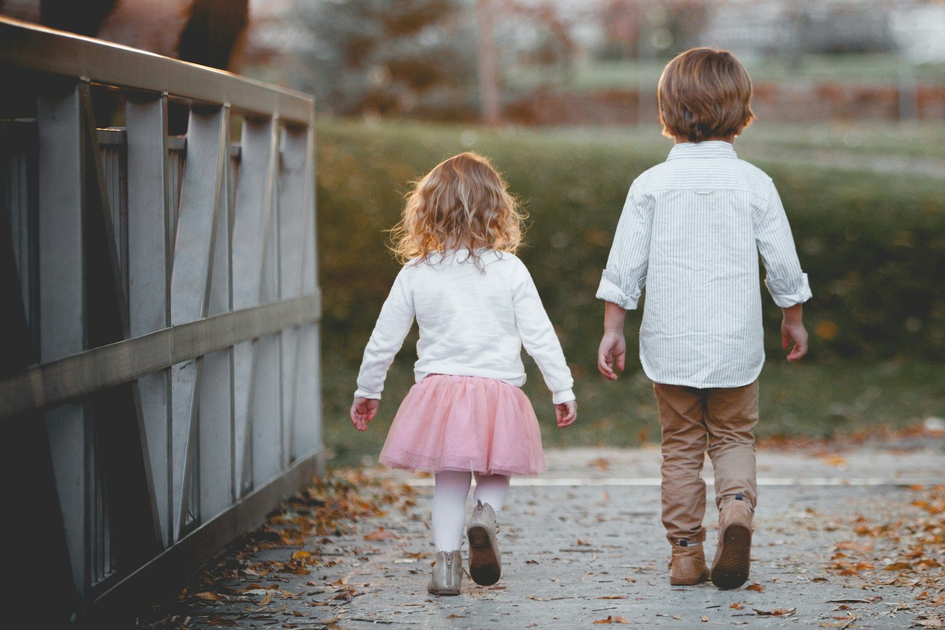 A boy and a girl are walking down a sidewalk holding hands.