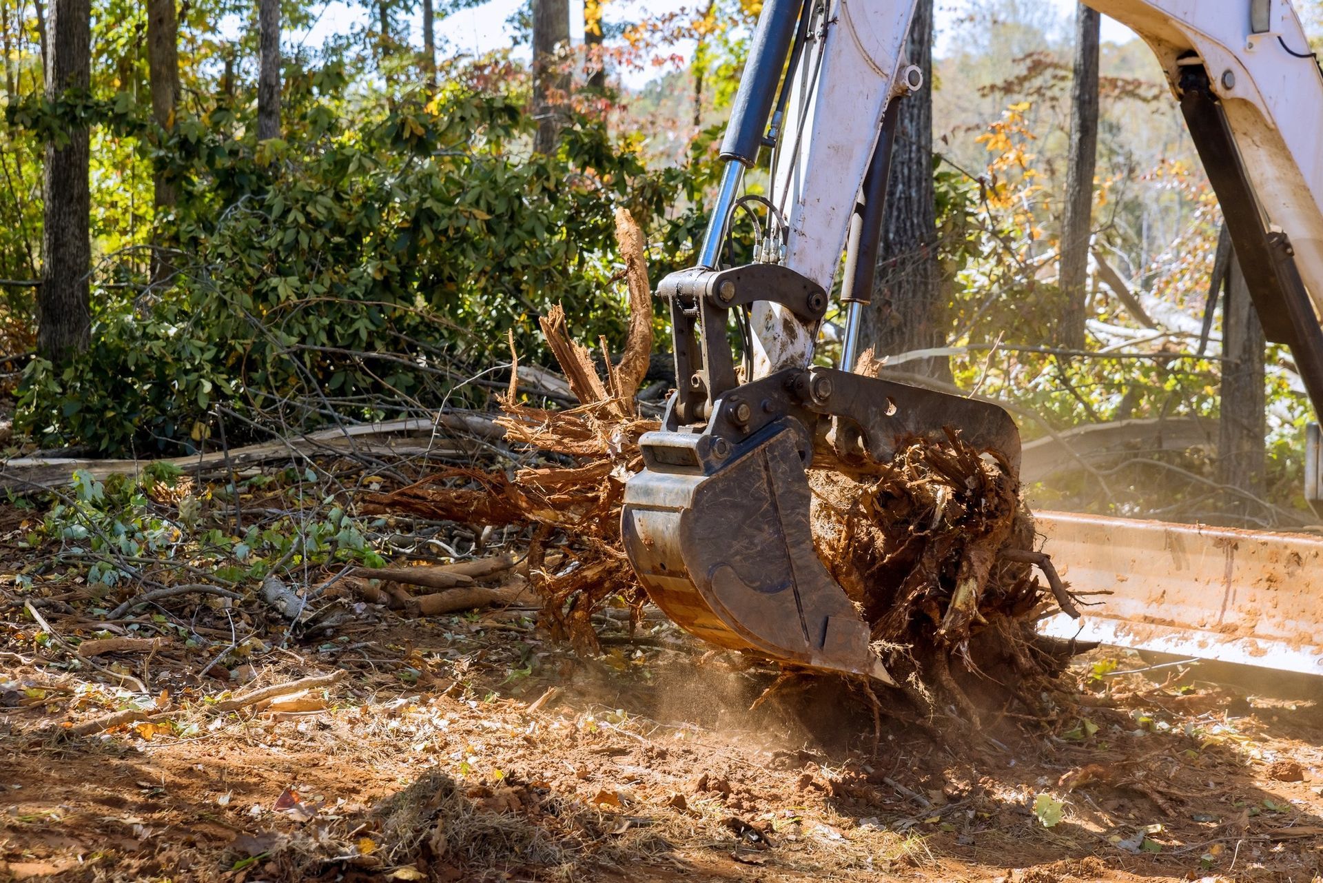 An excavator removing a tree stump with dirt and debris flying in the air.