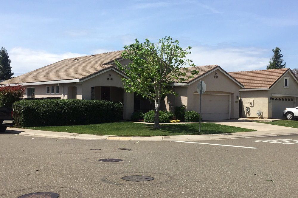 Suburban house with beige siding, a brown tiled roof, and a green front yard on a sunny day.
