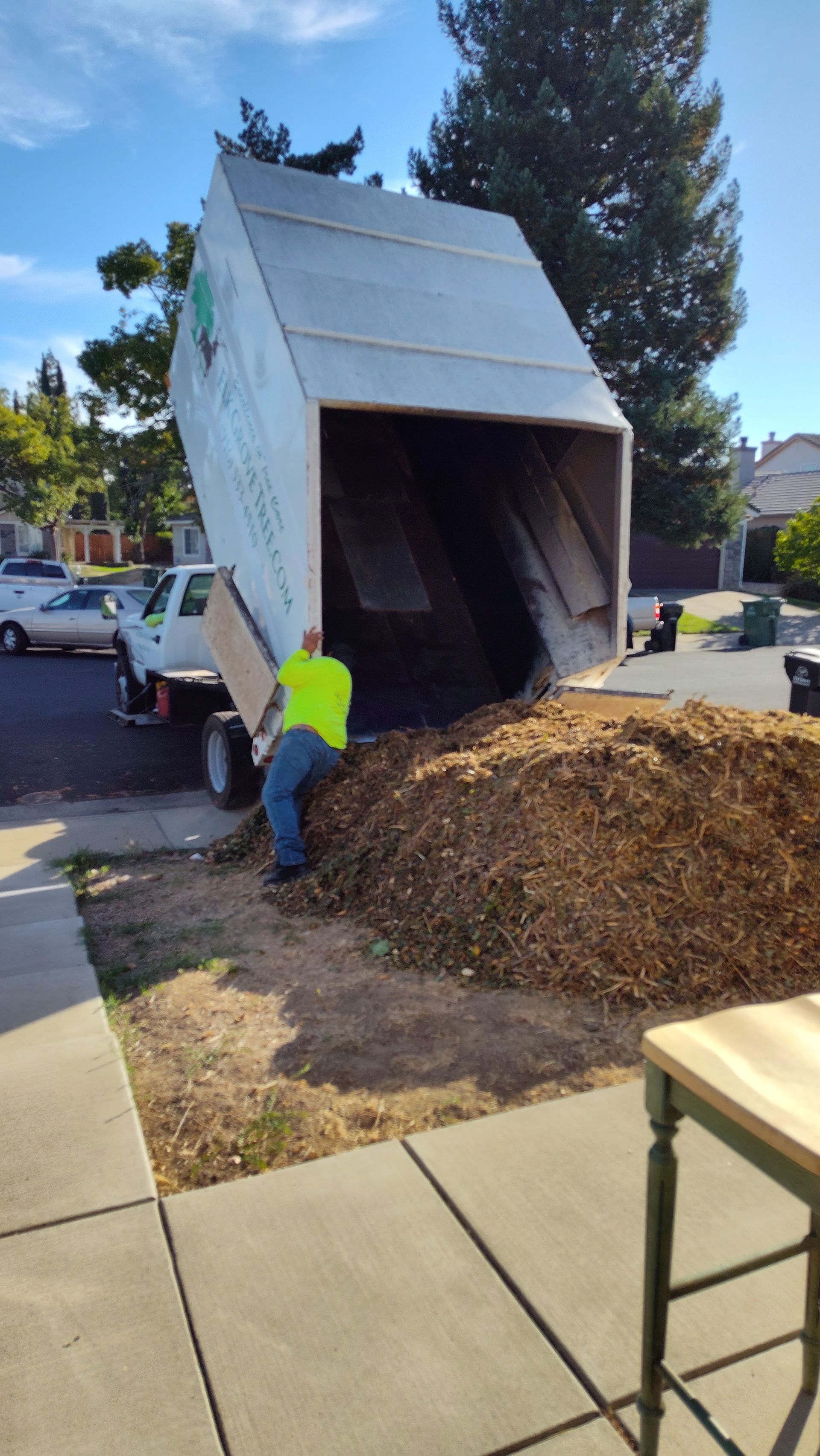 Man unloading wood chips from a truck into a yard on a sunny day.