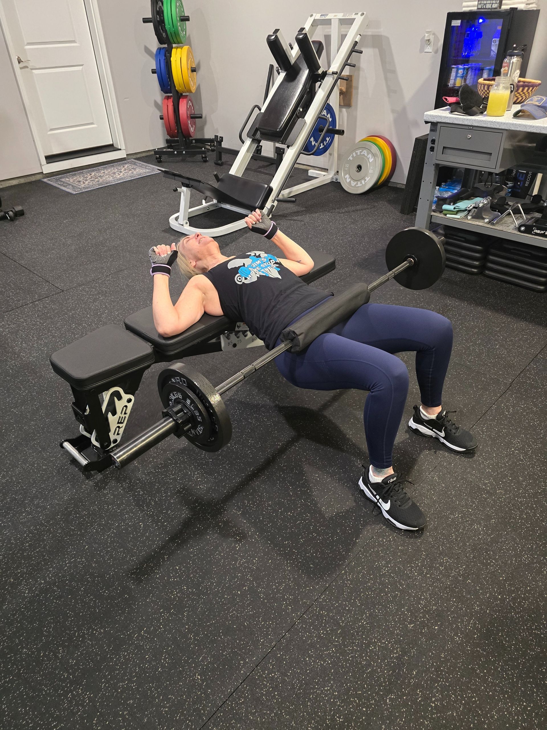 Person exercising on a stair stepper machine in a home gym. Leaning forward, holding handlebars. Black machine, dark clothing.