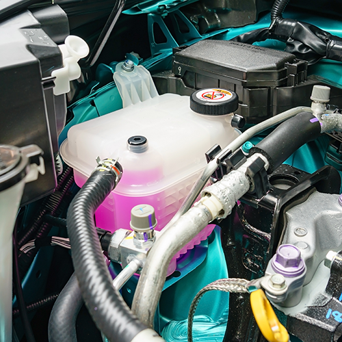 Car engine bay with pink coolant reservoir, black hoses, and visible metal components