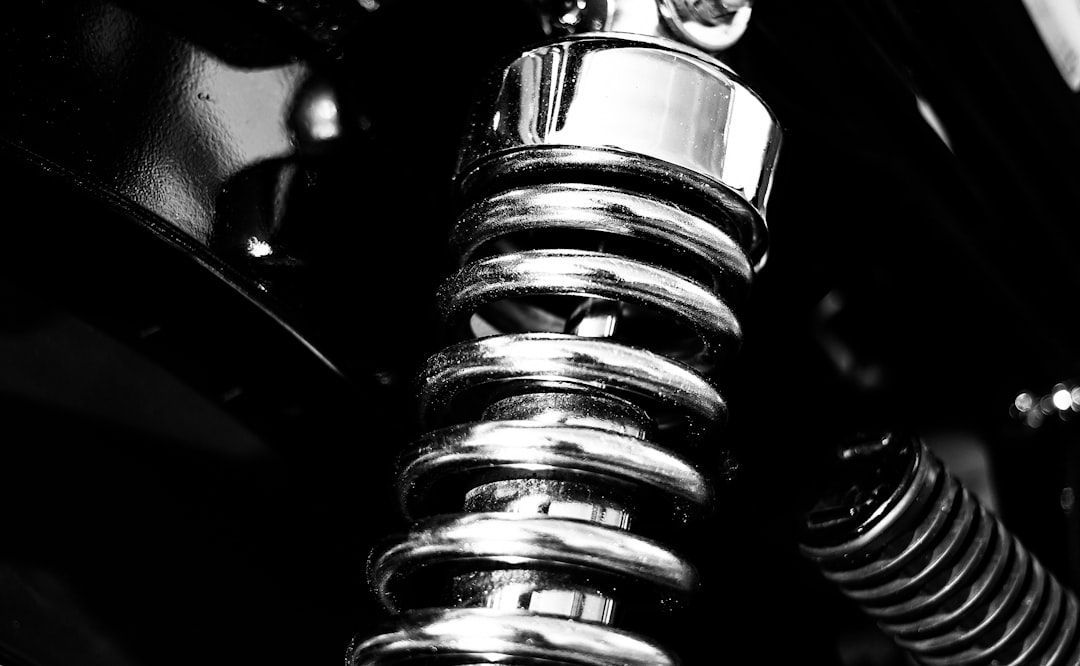 Close-up of a chrome coil spring on a dark mechanical component, lit dramatically in black and white.