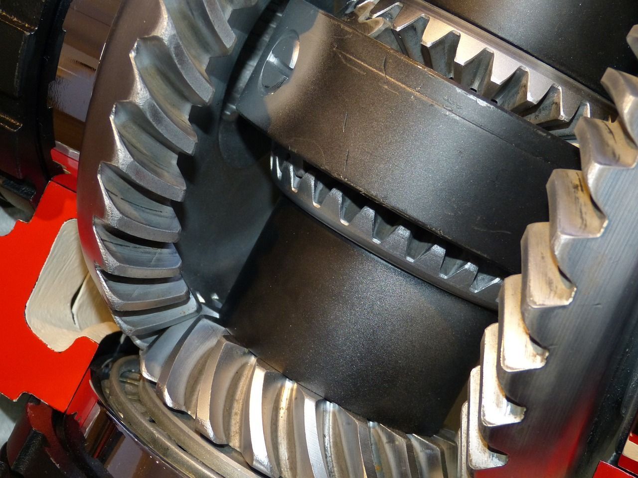 Close-up of shiny metal gears interlocking inside a machine, with a red component in the background