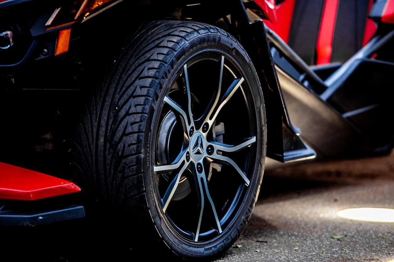 Close-up of a black sports car wheel with red body accents on a dark surface