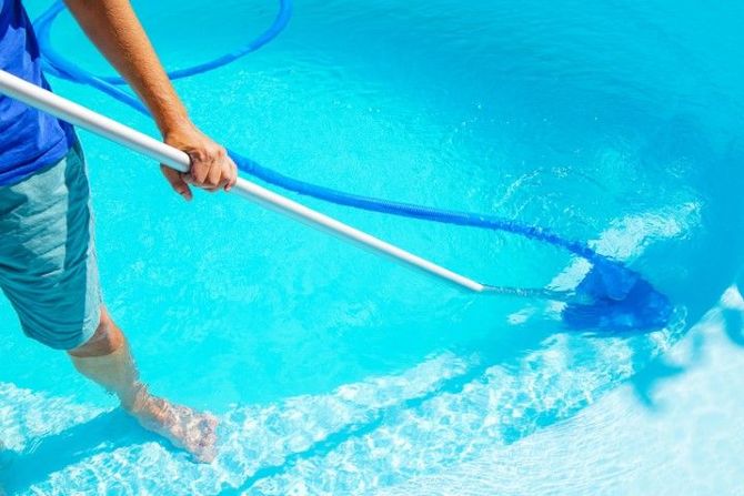 Person using a pool net to skim a bright blue swimming pool