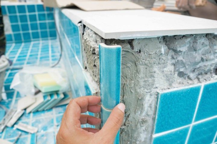 Hand placing a blue tile on a wall during bathroom tiling work
