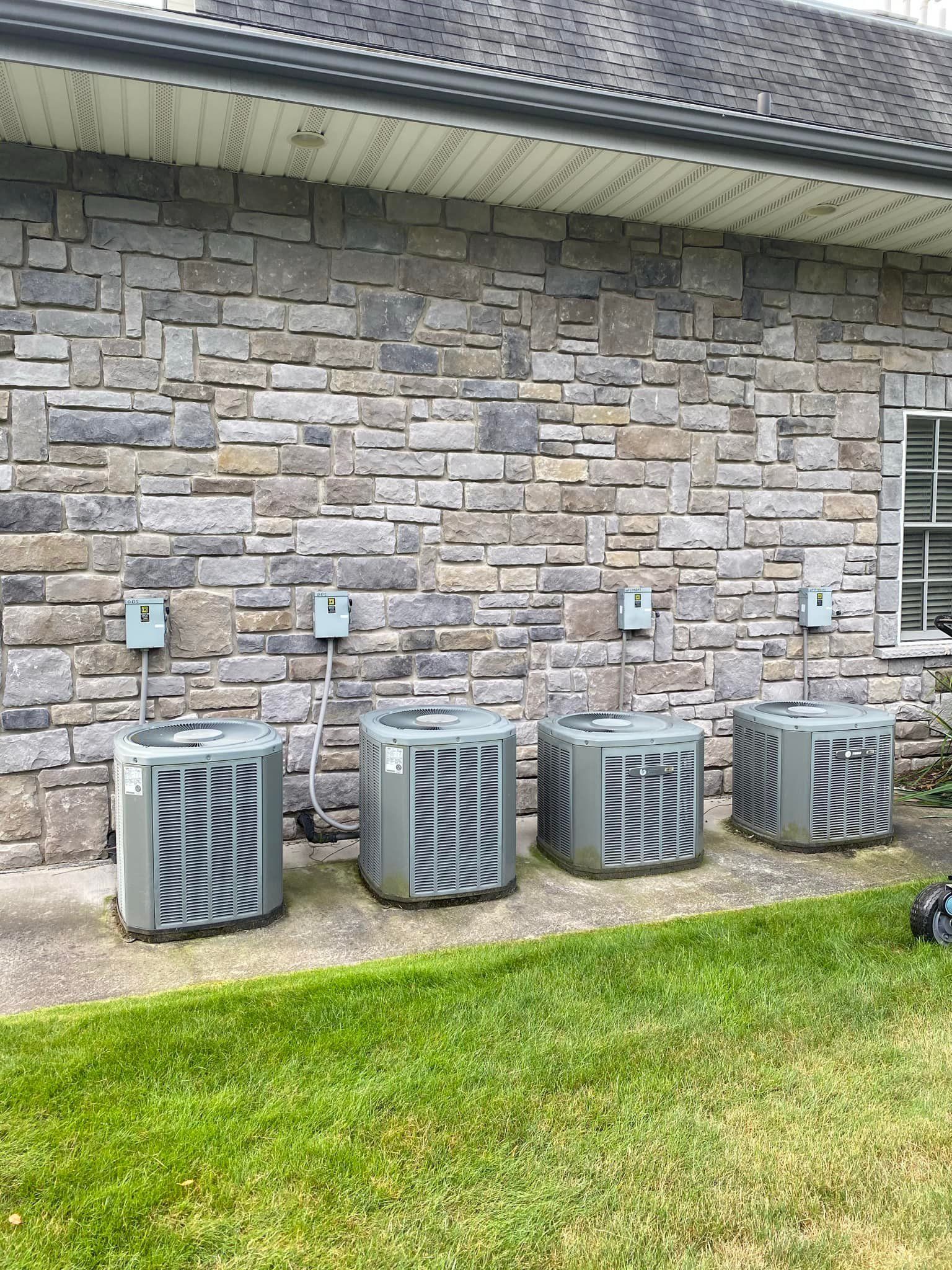 A row of air conditioners are sitting in front of a brick building.