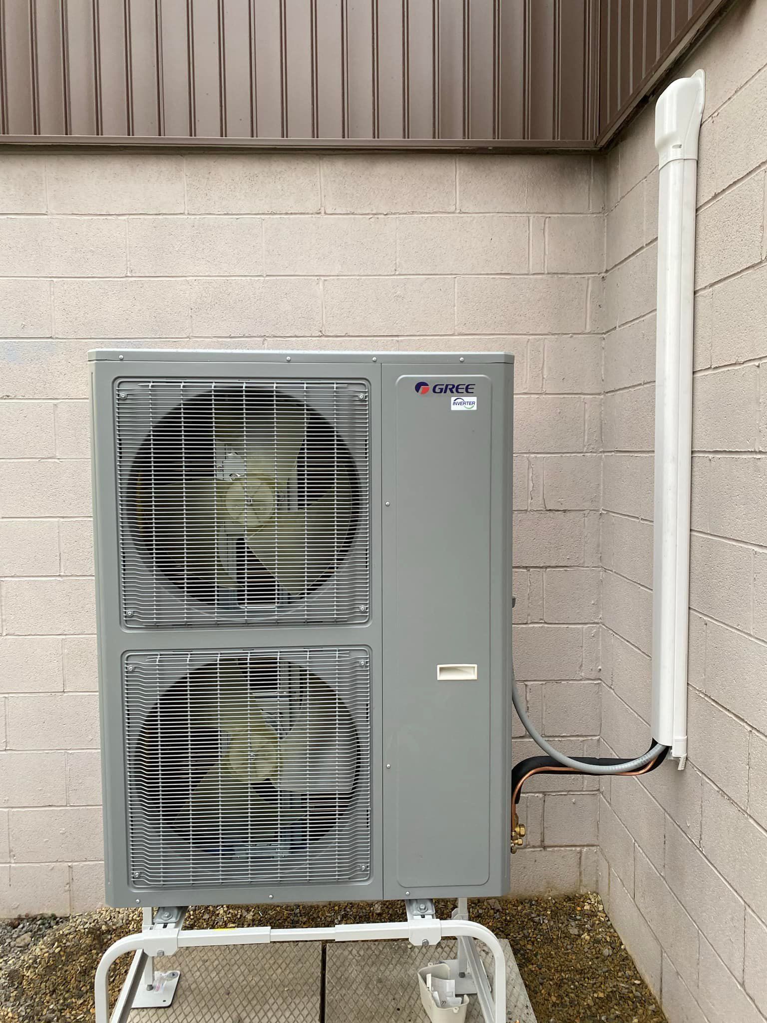 A large air conditioner is sitting outside of a brick building.