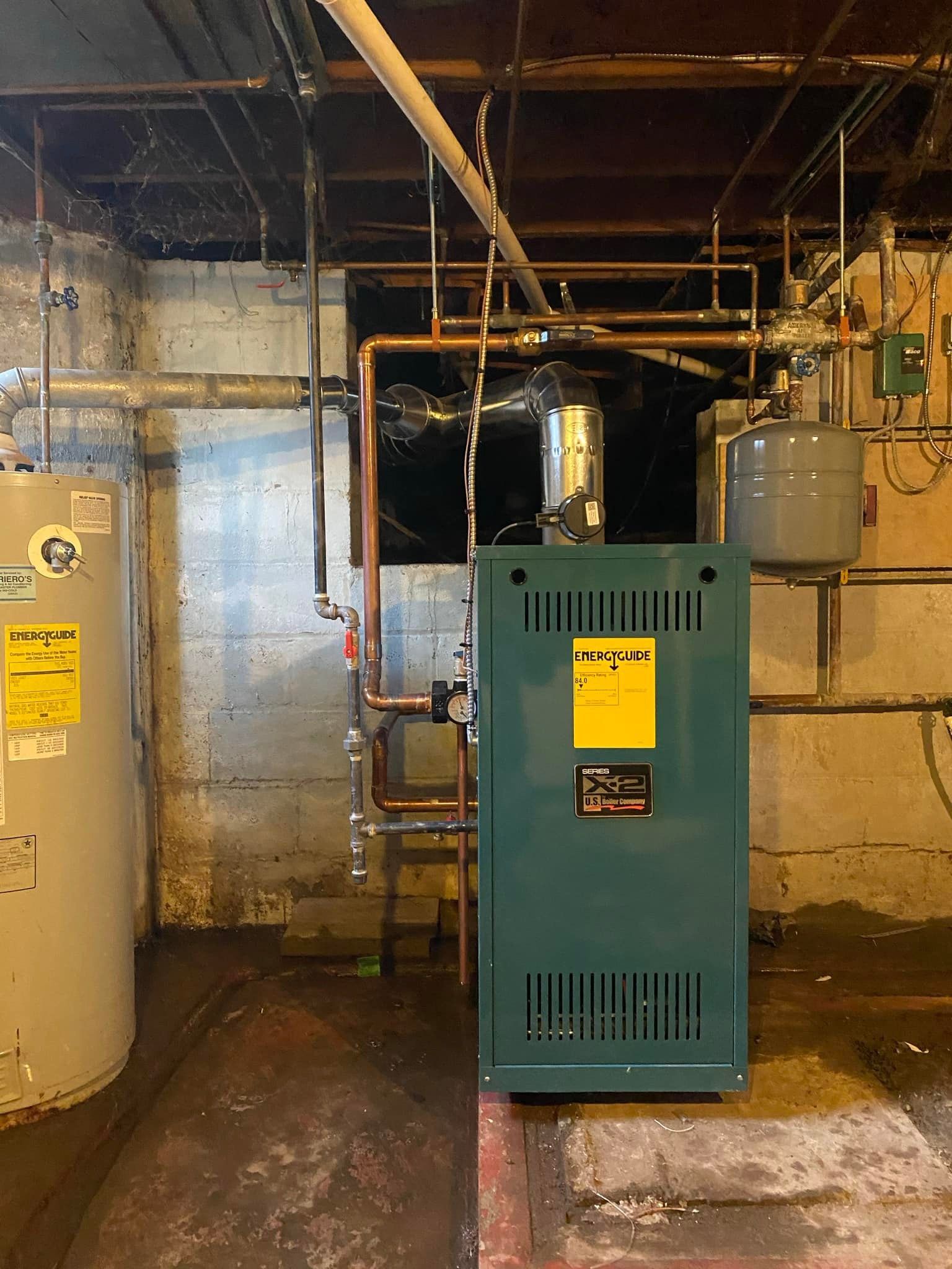 A green boiler is sitting in a basement next to a water heater.