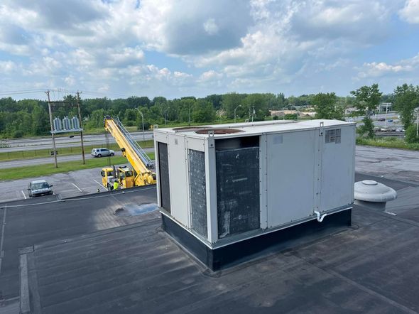 A large white box is sitting on top of a roof next to a crane.