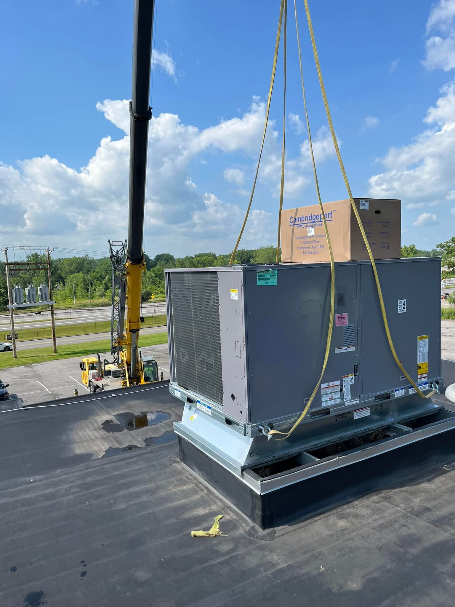 A crane is lifting a large air conditioner on top of a roof.