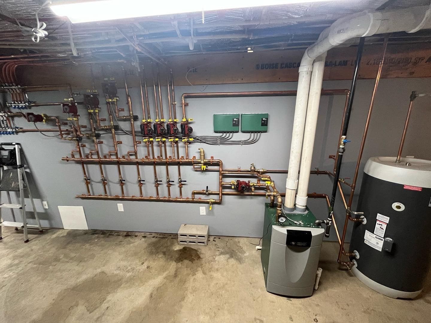 A boiler is sitting in a basement next to a water heater.