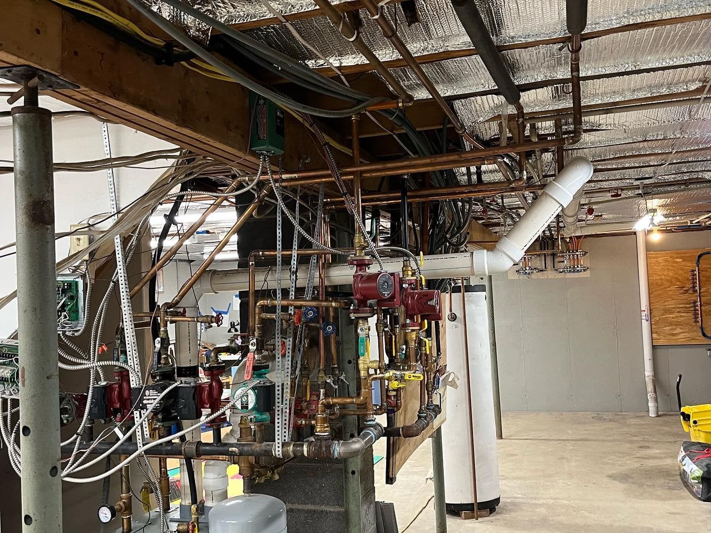 A basement with a lot of pipes and wires hanging from the ceiling.