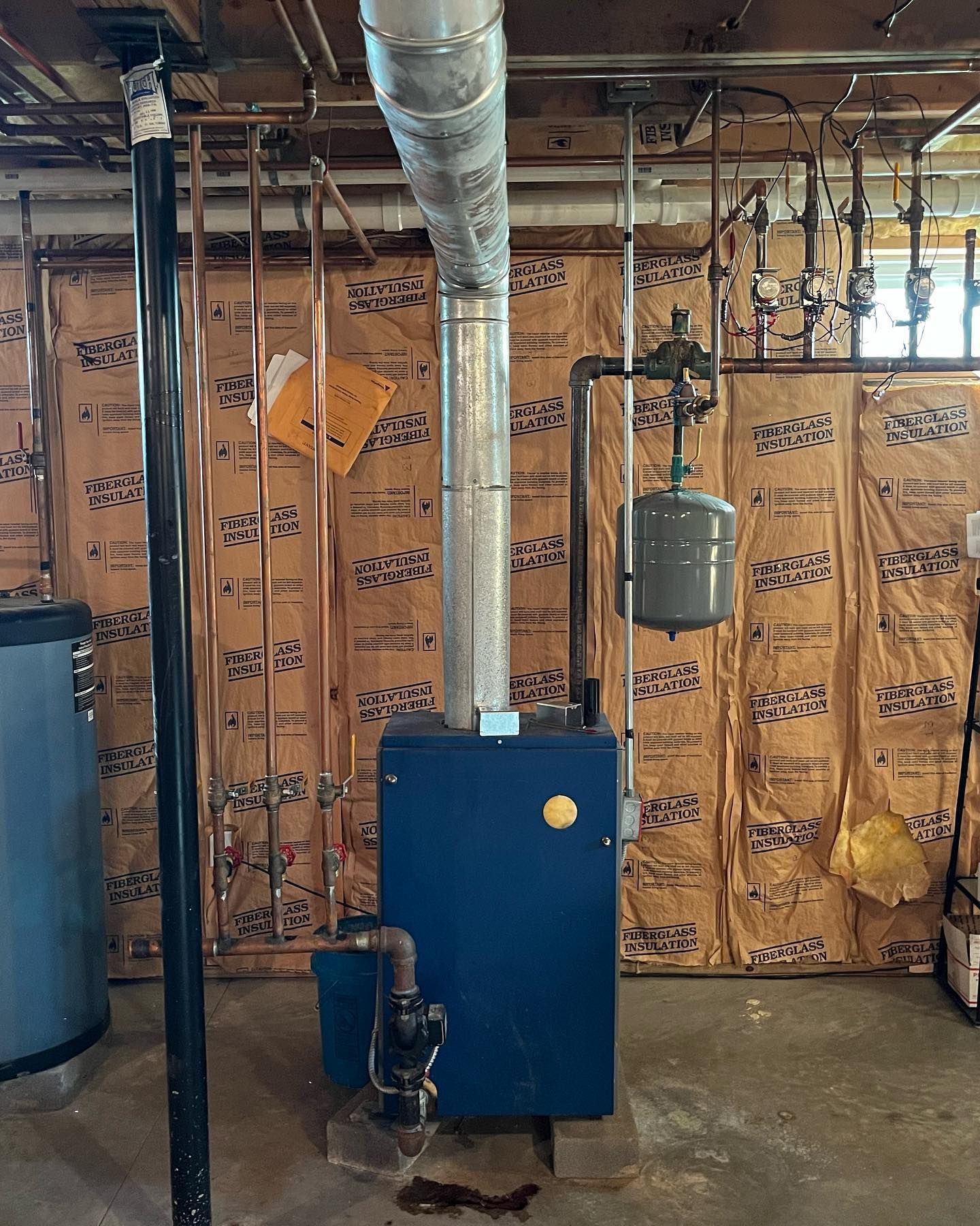 A blue boiler is sitting in a basement next to a water heater.